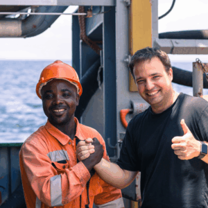 Two seafarers on ship smiling and shaking hands, symbolizing teamwork, safety culture, and cooperation promoted by OJ Safety during inspections and onboard training.