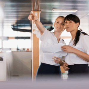 Two female ship officers on the bridge discussing navigation plan and safety procedures, symbolizing leadership, communication, and maritime safety culture.