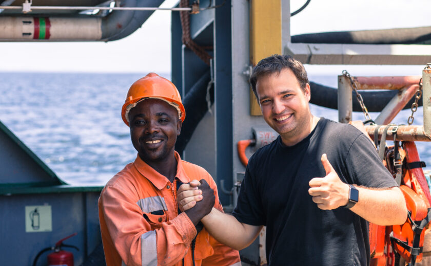 Two seafarers on ship smiling and shaking hands, symbolizing teamwork, safety culture, and cooperation promoted by OJ Safety during inspections and onboard training.
